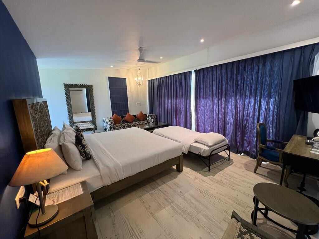 A hotel room with two beds, a desk, a chair, a TV, and a chandelier.