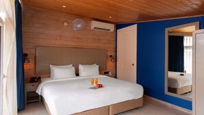 A hotel room with a wooden ceiling, a large bed with white bedding, a bedside table with a lamp, and a mirror on the wall.