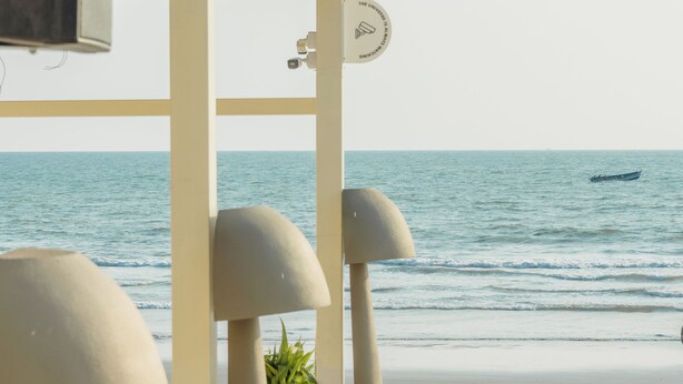 A beachside seating area with white lounge chairs and tables, overlooking the ocean.