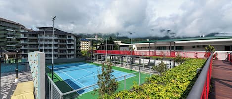 Una cancha de tenis con una pared de escalada, rodeada de edificios y vegetación.