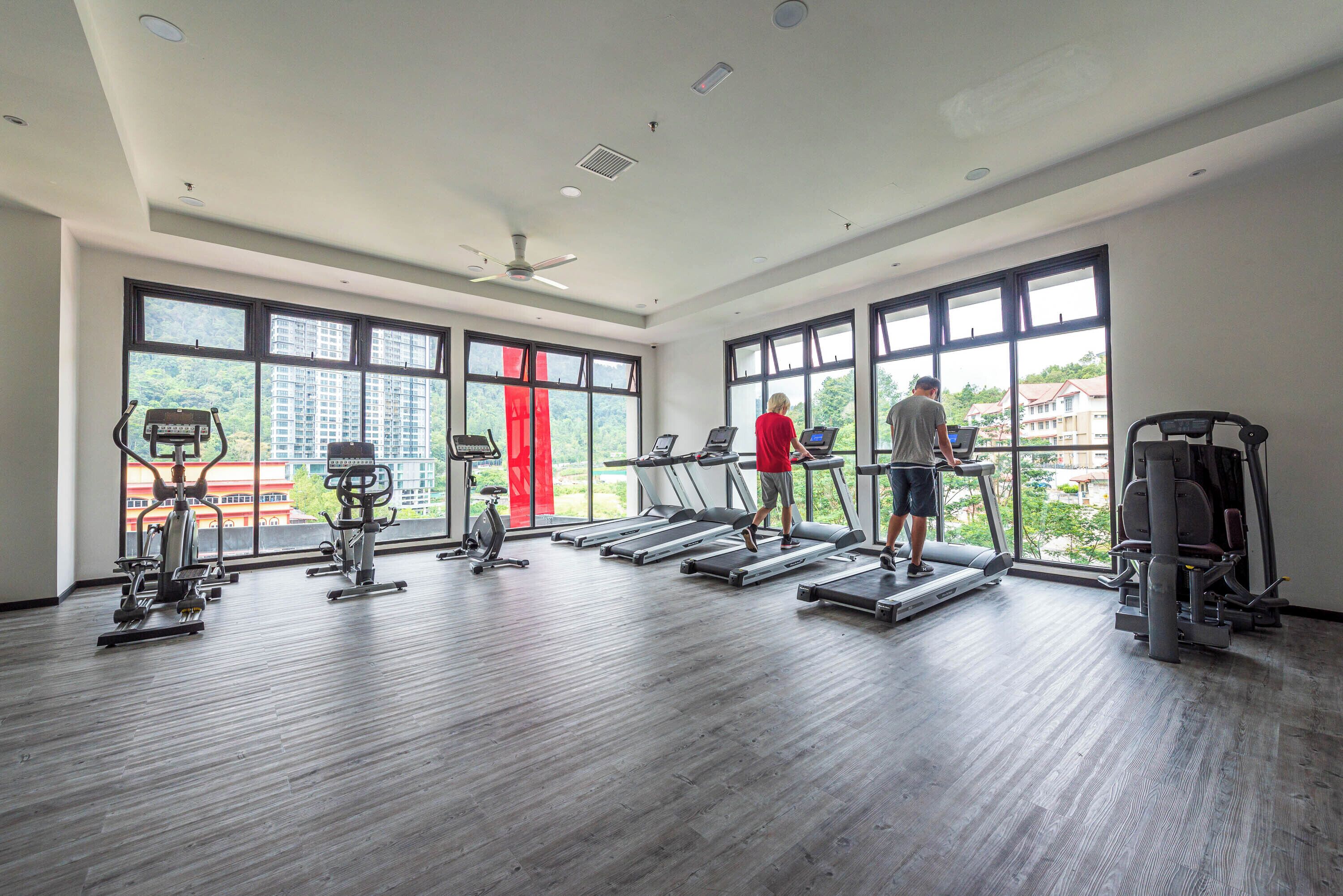 Een fitnessruimte met loopbanden, hometrainers en een rode wand.