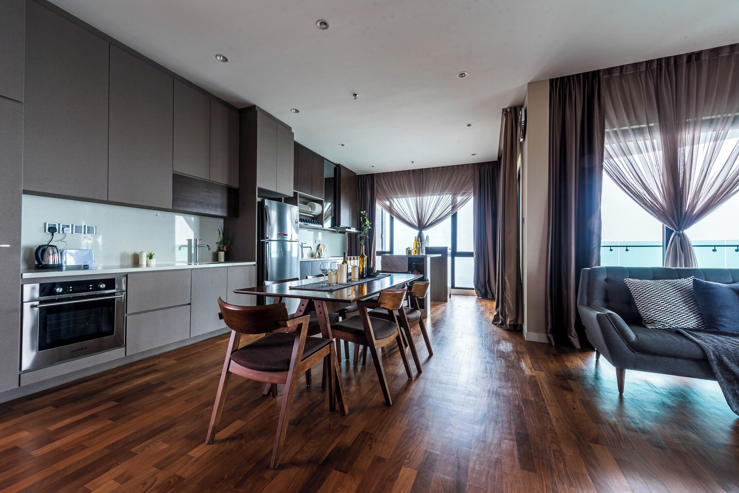 A modern kitchen with a dining area, wooden flooring, and a view of the outdoors.