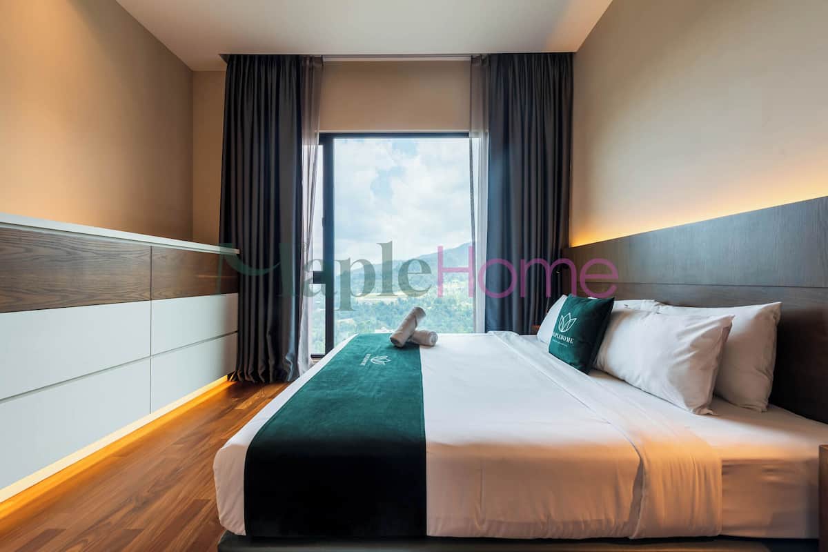 A hotel room with a large bed, a view through the window, and a wooden floor.