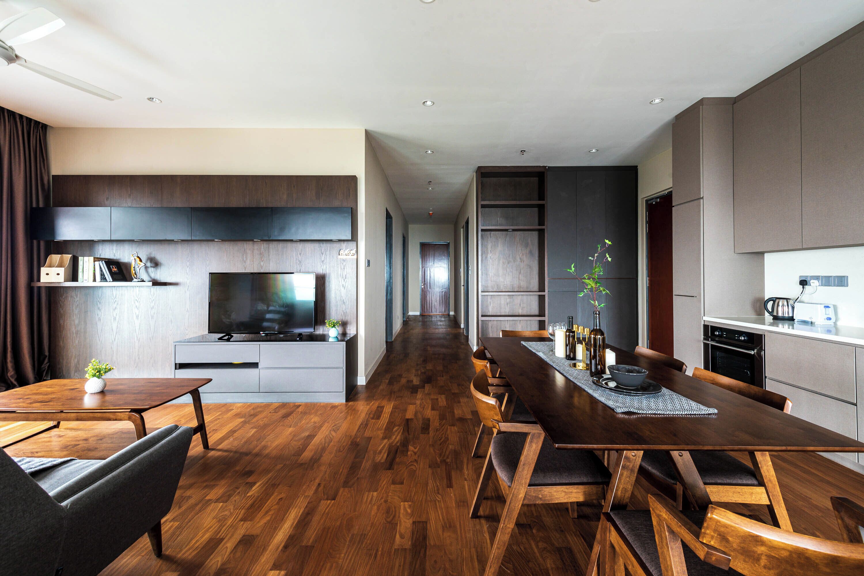 Una cocina moderna con televisor de pantalla plana, armarios de madera y un comedor con una mesa larga y sillas.