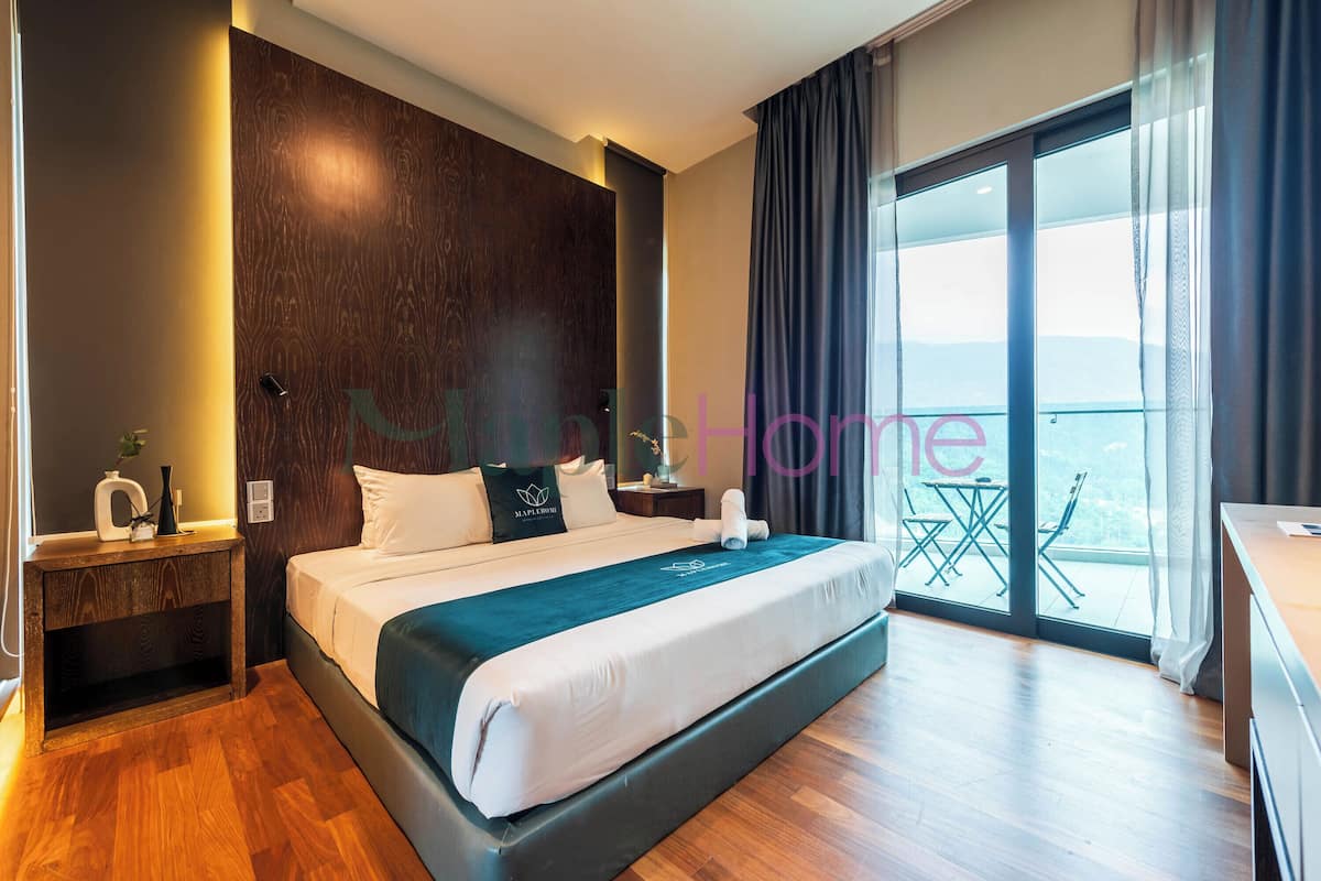 A modern hotel room with a large bed, wooden paneling, a balcony with a table and chairs, and a view of the outdoors.
