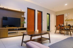 A modern living room with a flat-screen TV, wooden furniture, a dining area with chairs and a table, and a kitchen visible through an open door. - Geo38 Premier Suites Genting Highlands (Genting Highlands)