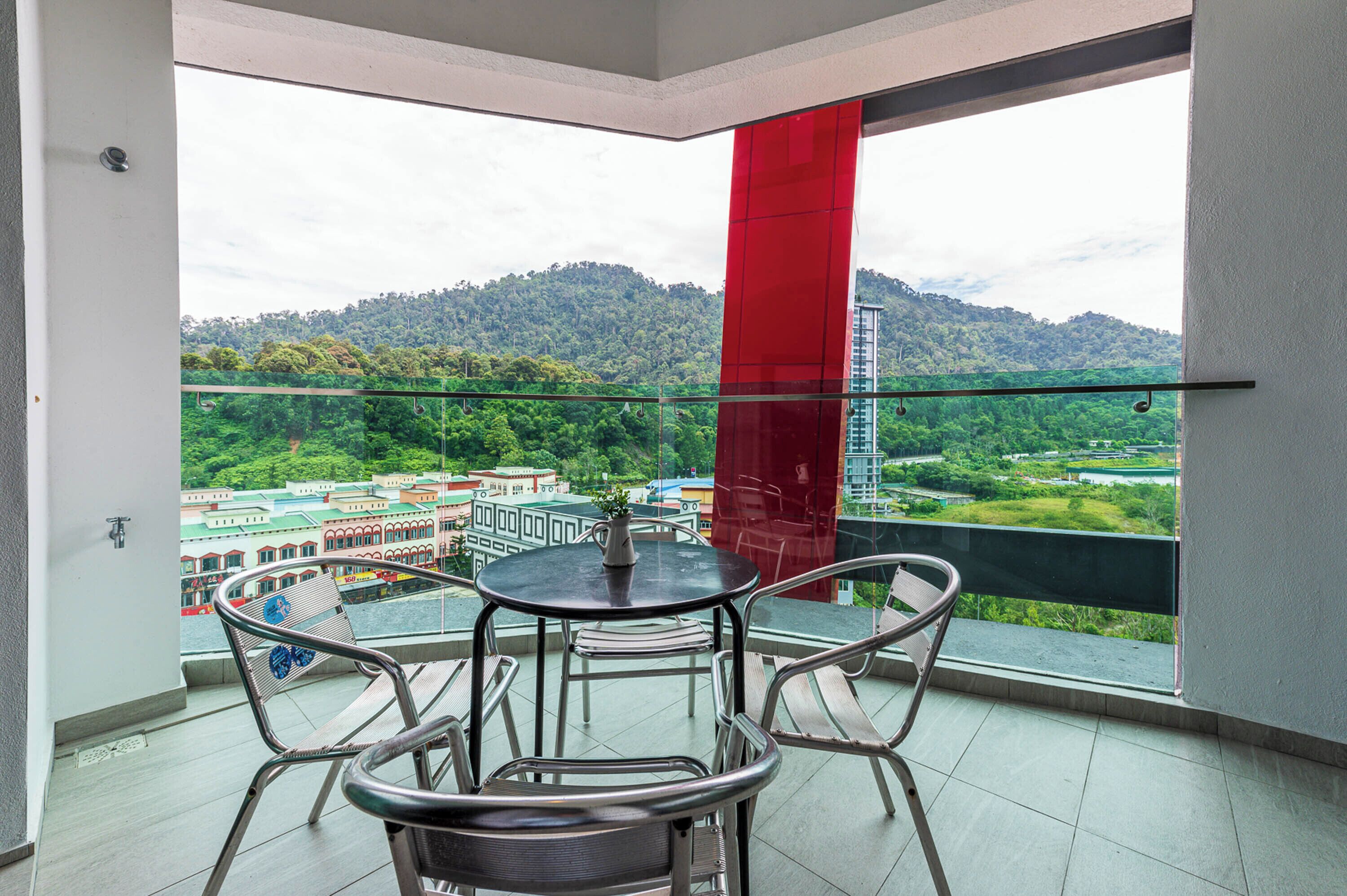 A balcony with a table and chairs, a glass railing, and a view of a cityscape and mountains.