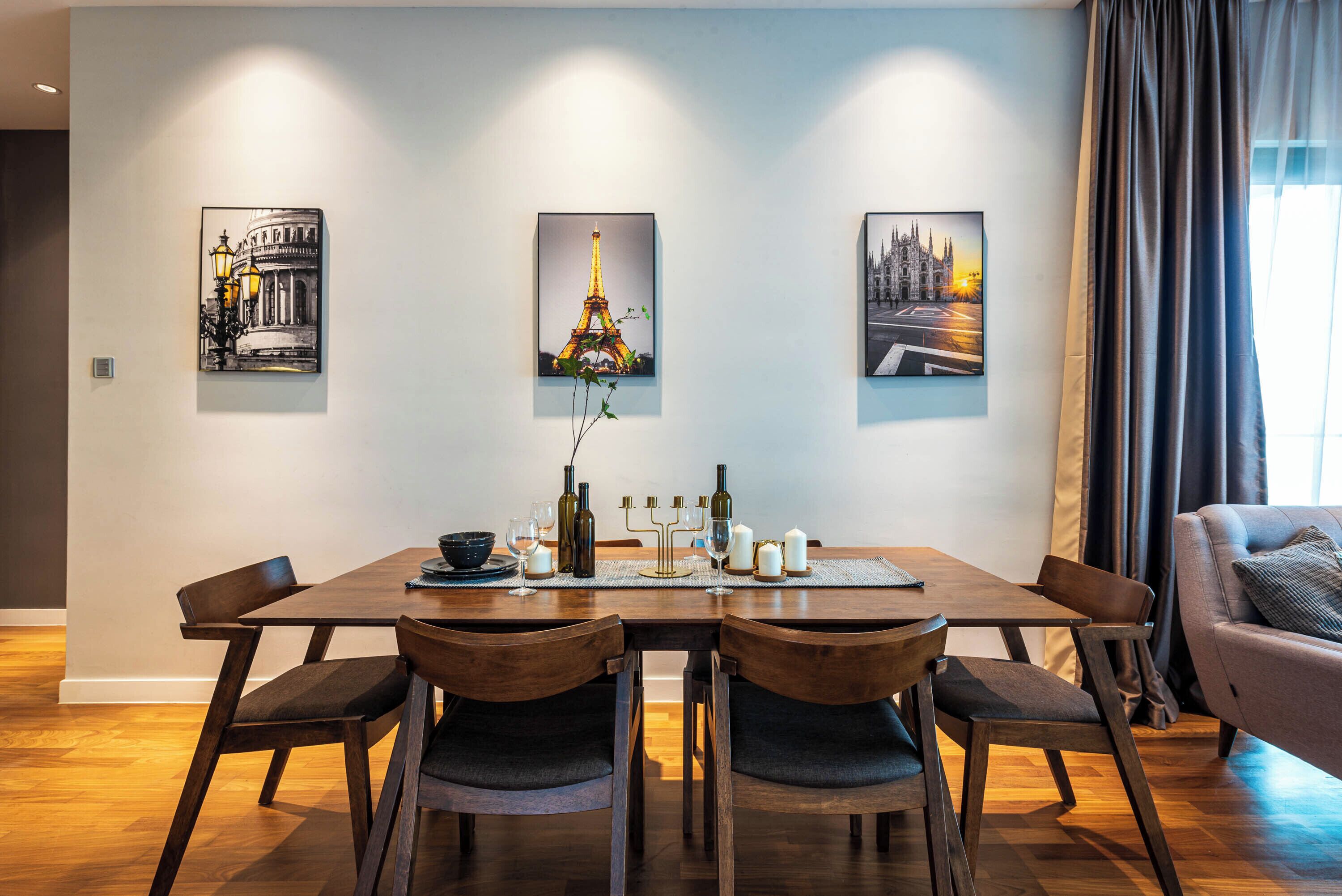 Uma sala de jantar com uma mesa de madeira, cadeiras e três quadros na parede.