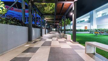 A covered walkway with a checkered floor, metal columns, and a green lawn area.