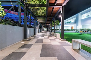 A covered walkway with a checkered floor, metal columns, and a green lawn area.