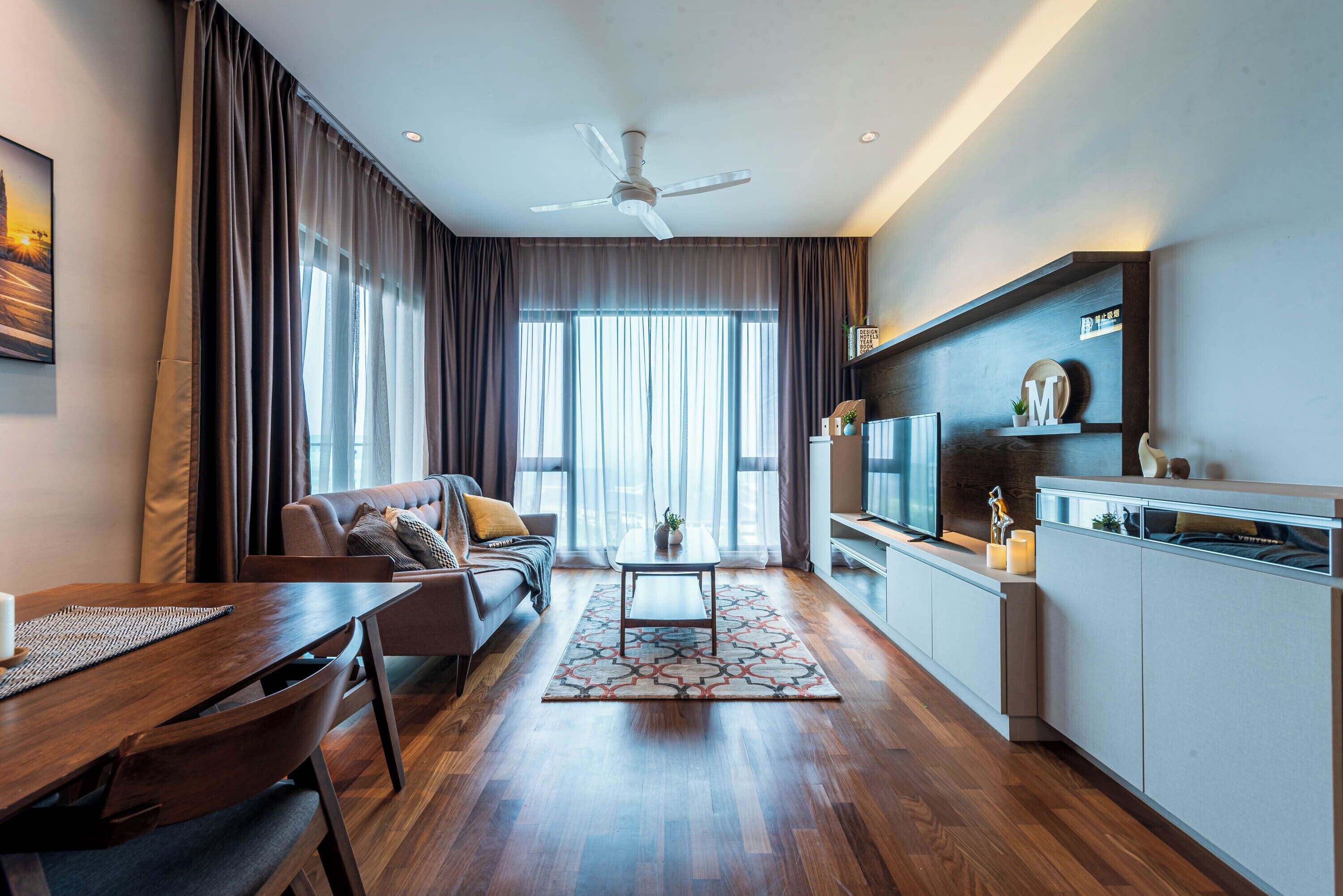 Una sala moderna con sofá, mesa de centro y comedor. Se observa una cocina con televisor y alacenas.