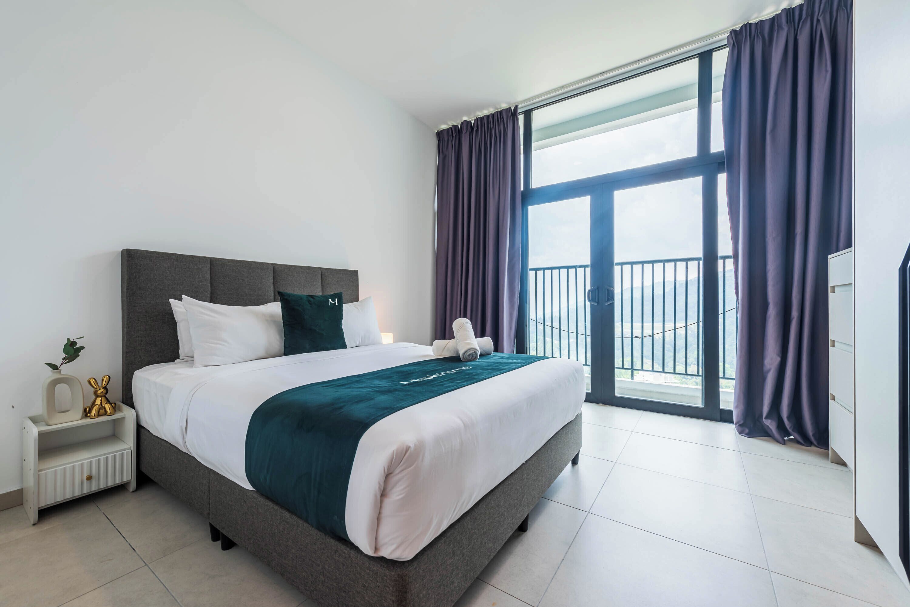 A modern hotel room with a large bed, a nightstand, a dresser, and a balcony with curtains.