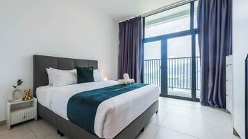 A modern hotel room with a large bed, a nightstand, a dresser, and a balcony with curtains.