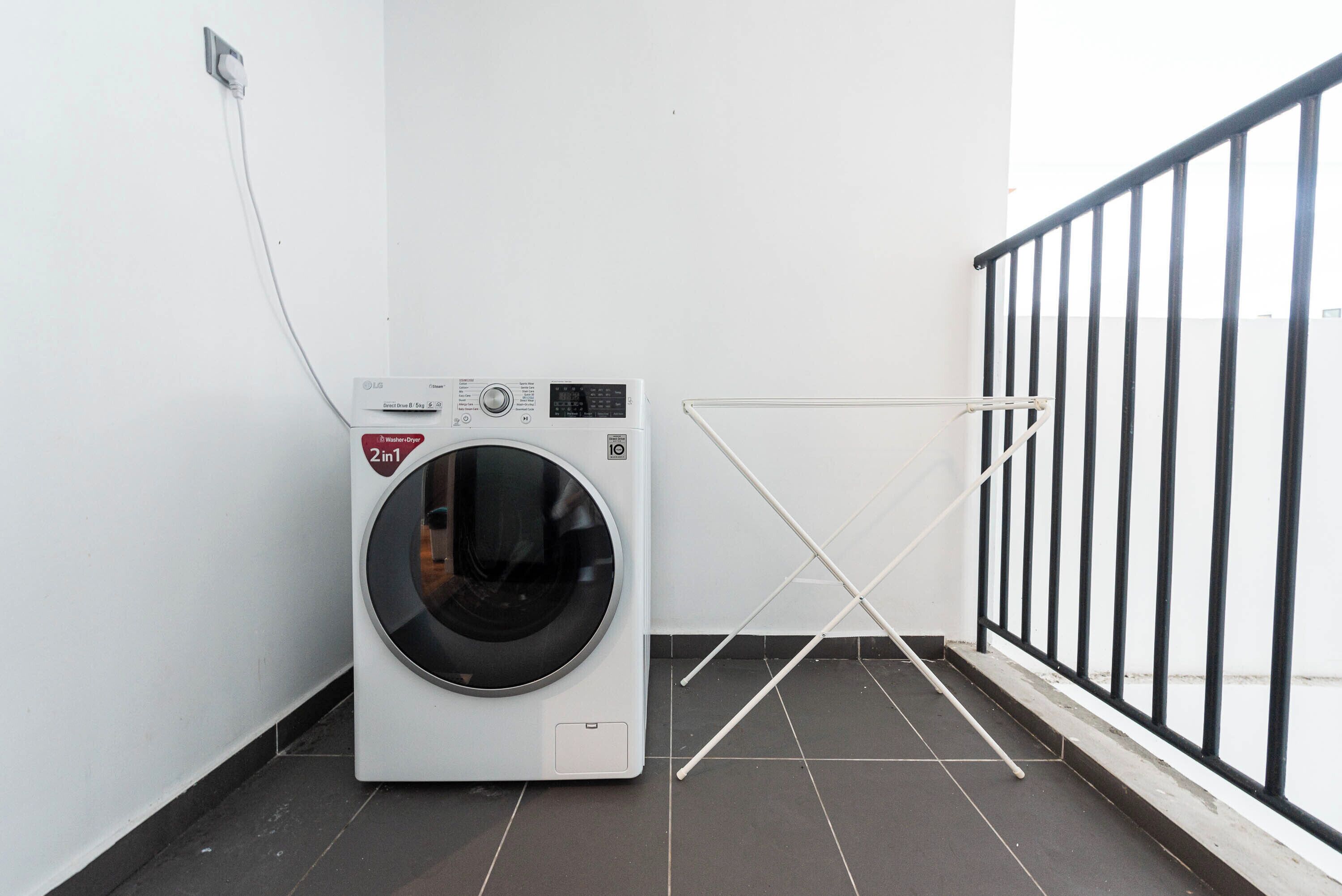 Una unidad compacta de lavadora-secadora en una esquina de una habitación con piso de baldosas y baranda de metal negro.