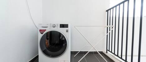 Un appareil compact combinant lave-linge et sèche-linge, placé dans un coin d’une pièce dont le sol est carrelé et qui est dotée d’une rambarde en métal noir.