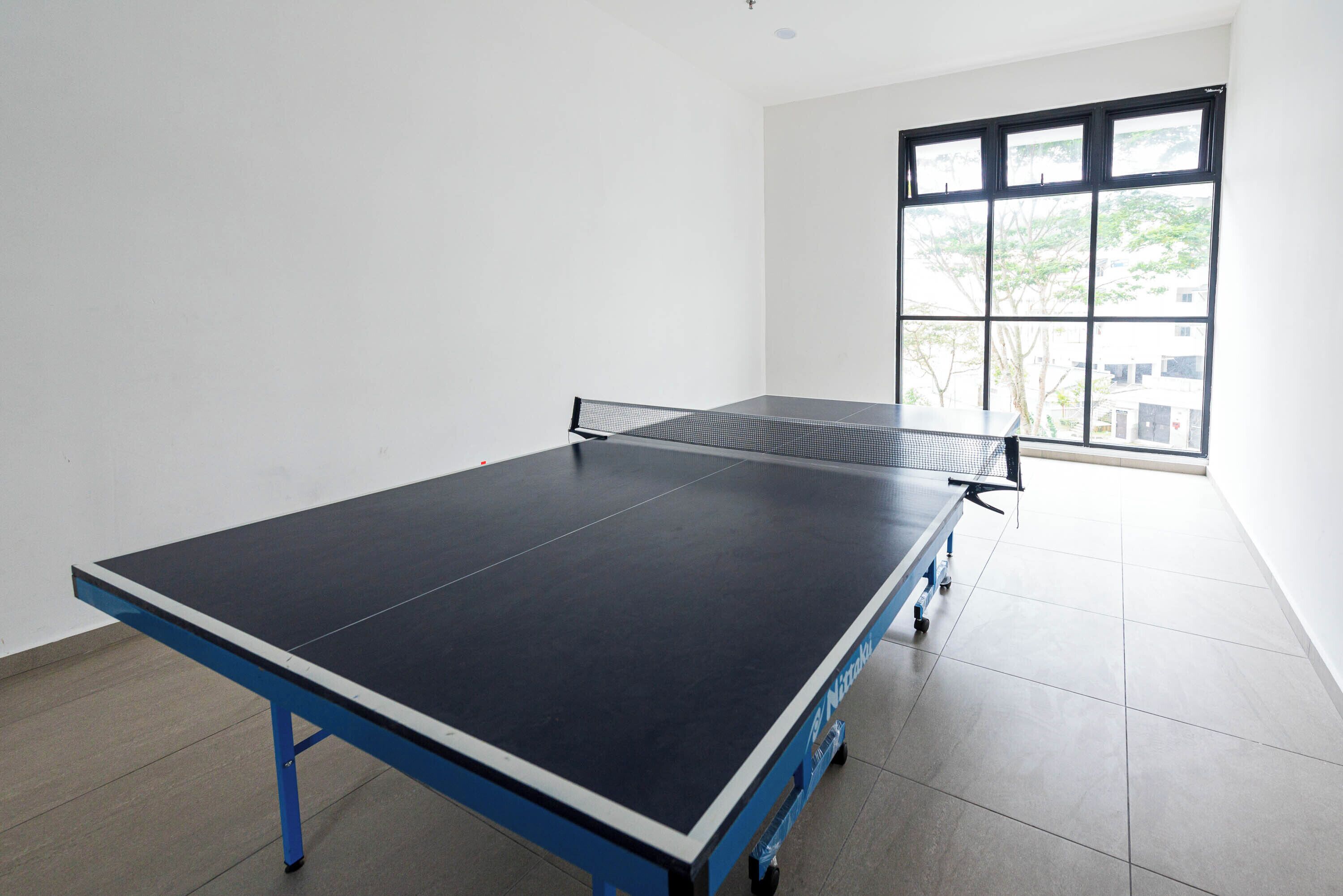 A ping pong table in a room with white walls and a large window.