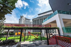 A playground with slides and climbing structures, surrounded by greenery and a red fence.