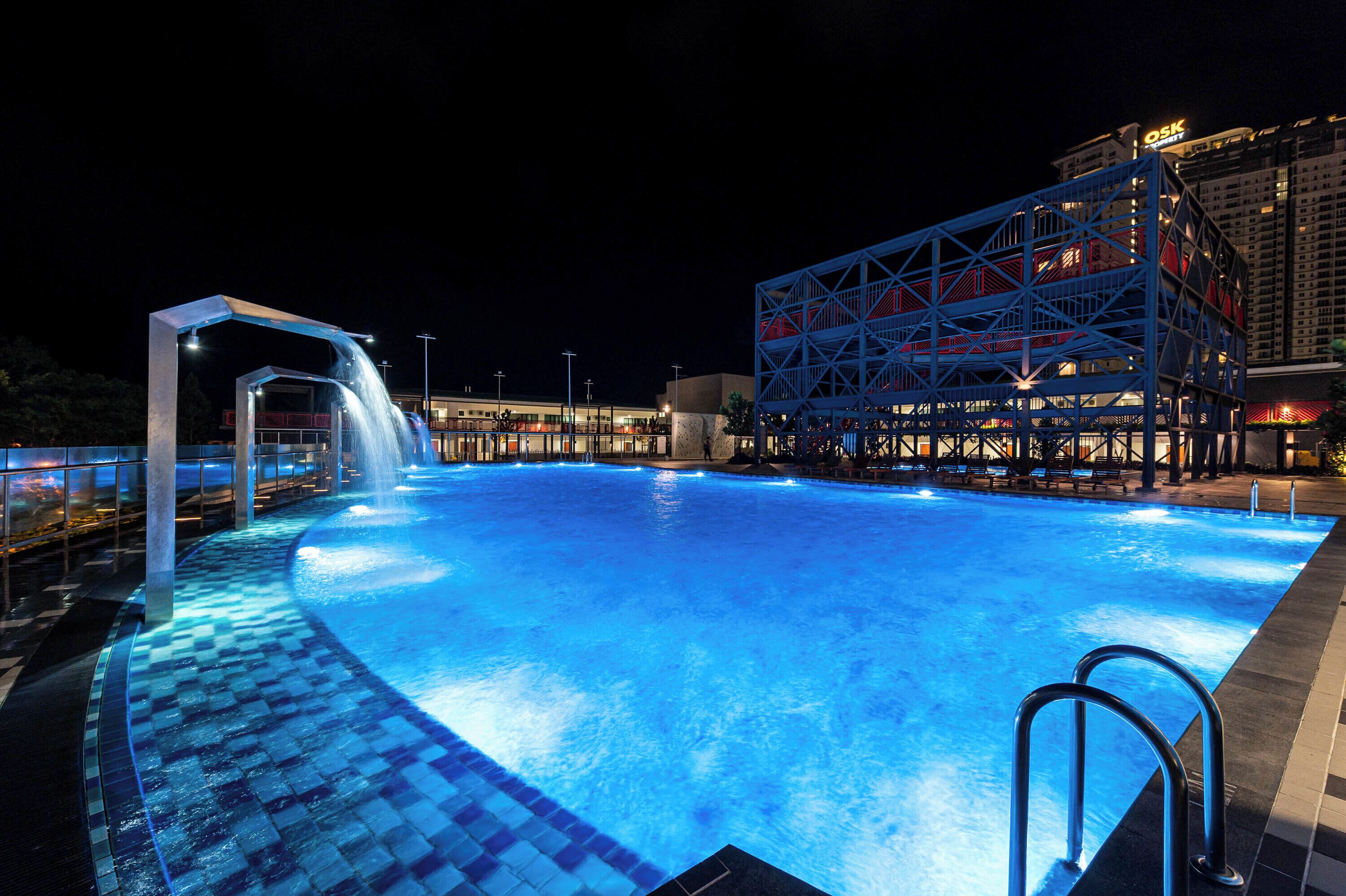 A swimming pool with a waterfall feature, surrounded by a modern building with a blue and red facade.