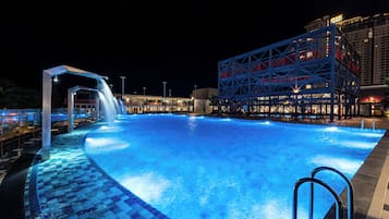 En swimmingpool med et vandfald, omgivet af en moderne bygning med en blå og rød facade.