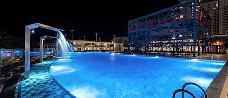 A swimming pool with a waterfall feature, surrounded by a modern building with a blue and red facade.