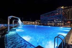 Une piscine agrémentée d’une cascade, entourée d’un bâtiment moderne à la façade bleue et rouge.