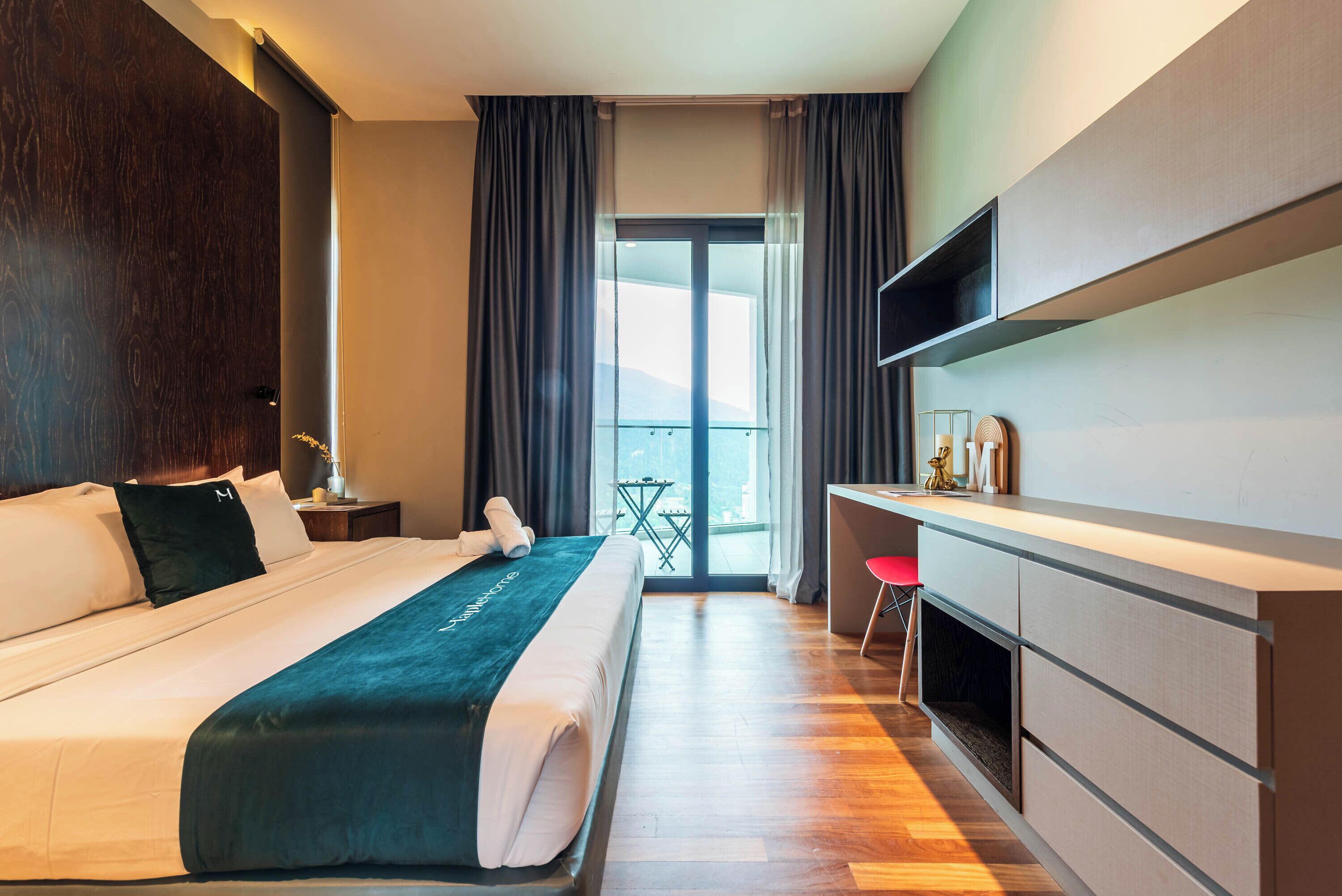A modern hotel room with a large bed, a desk, a TV, and a balcony with a view.