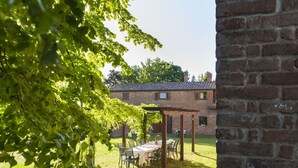 A patio area with a table and chairs, a pergola, and a brick building in the background.