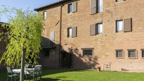 A brick building with a grassy courtyard, outdoor seating, and a tree.
