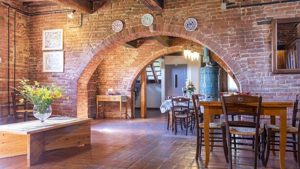 A rustic dining area with brick walls, wooden beams, and a large blue stove.