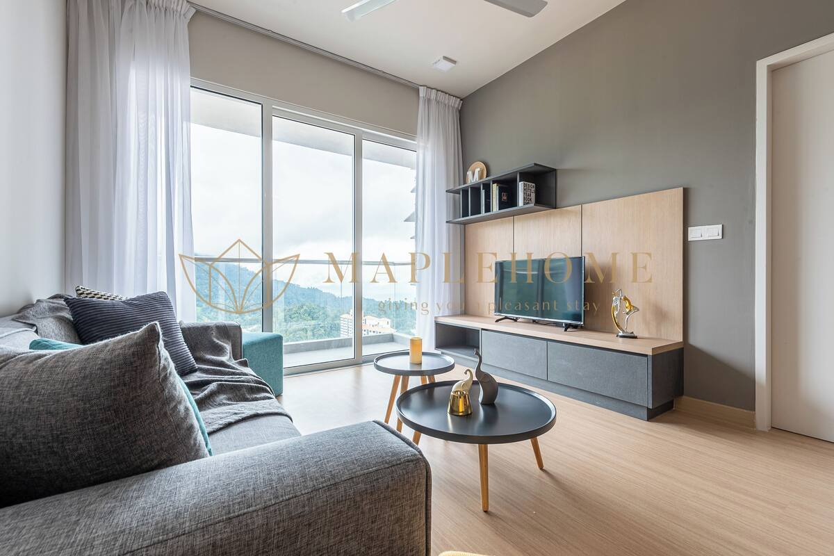 Un salon moderne avec un canapé, deux tables d’appoint, un téléviseur et une grande fenêtre avec des rideaux.