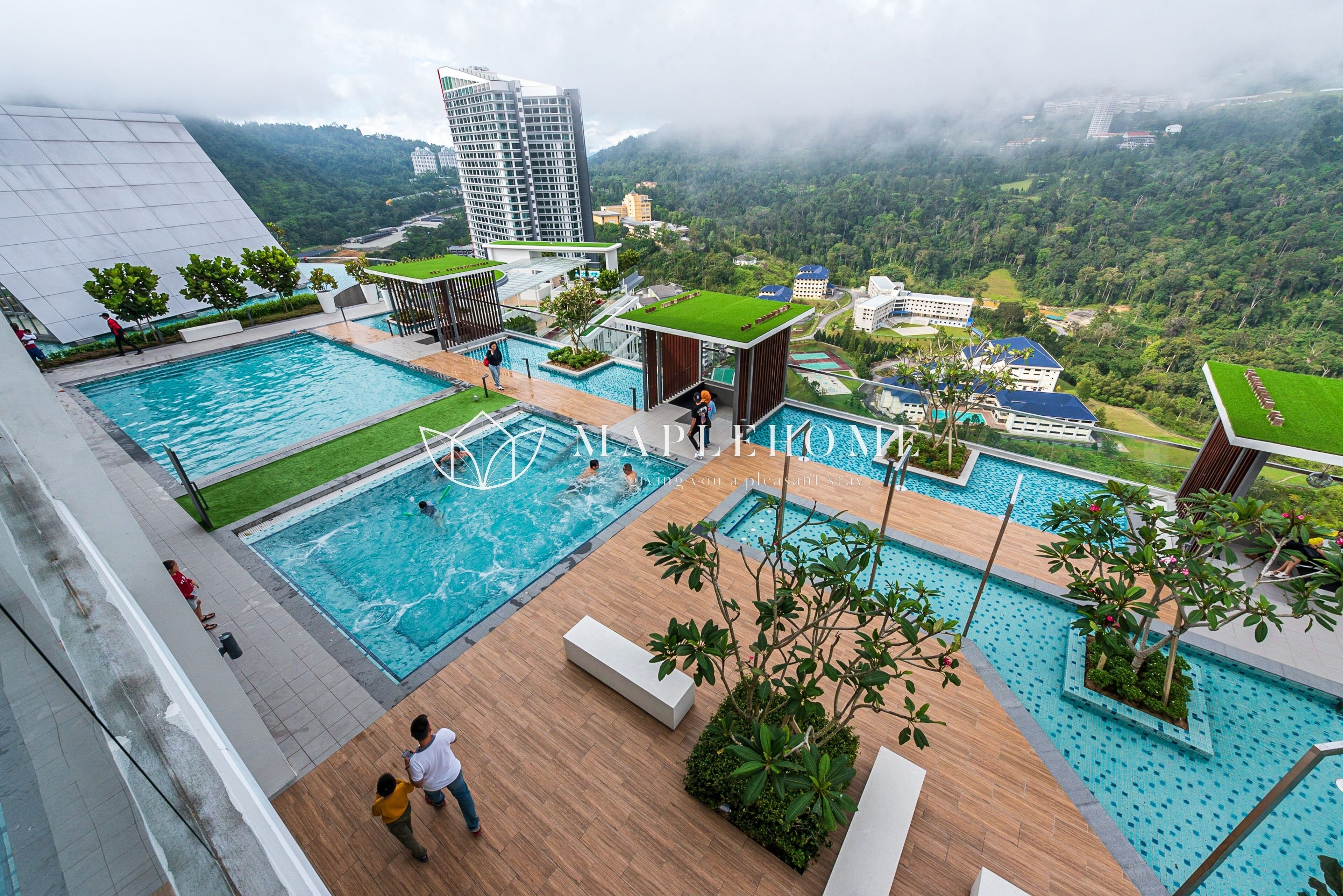 A rooftop pool area with multiple swimming pools, surrounded by greenery and overlooking a mountainous landscape.