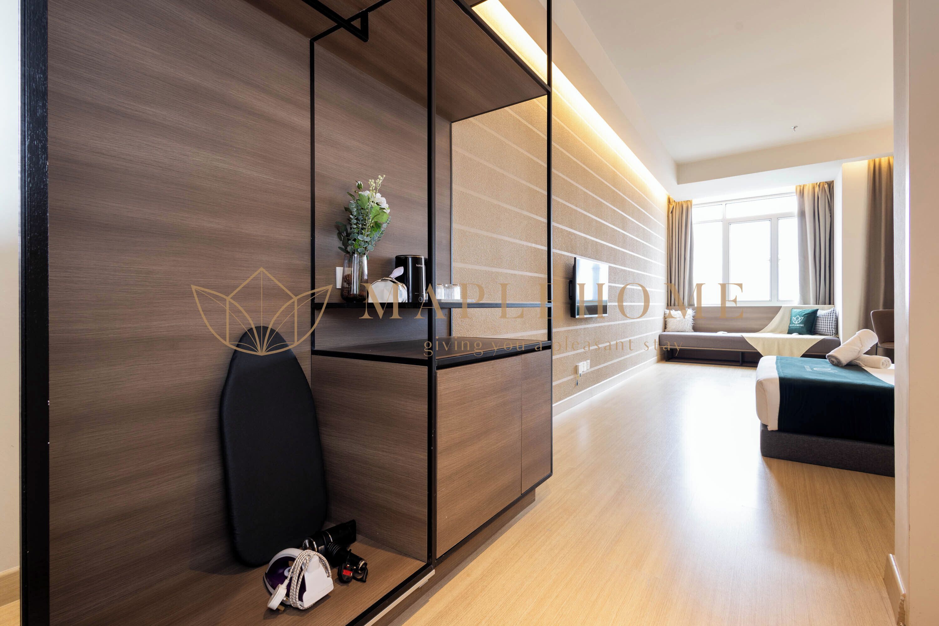 Una habitación de hotel moderna con una pared de acento de madera, un sofá negro, una cama con cubrecama verde y una mesita de noche con un jarrón y una planta.