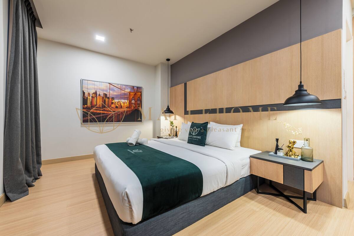 Une chambre d’hôtel moderne avec un lit soigneusement fait, un tableau représentant un paysage urbain accroché au mur, une table de chevet avec une lampe et une petite table de nuit agrémentée d’objets décoratifs.