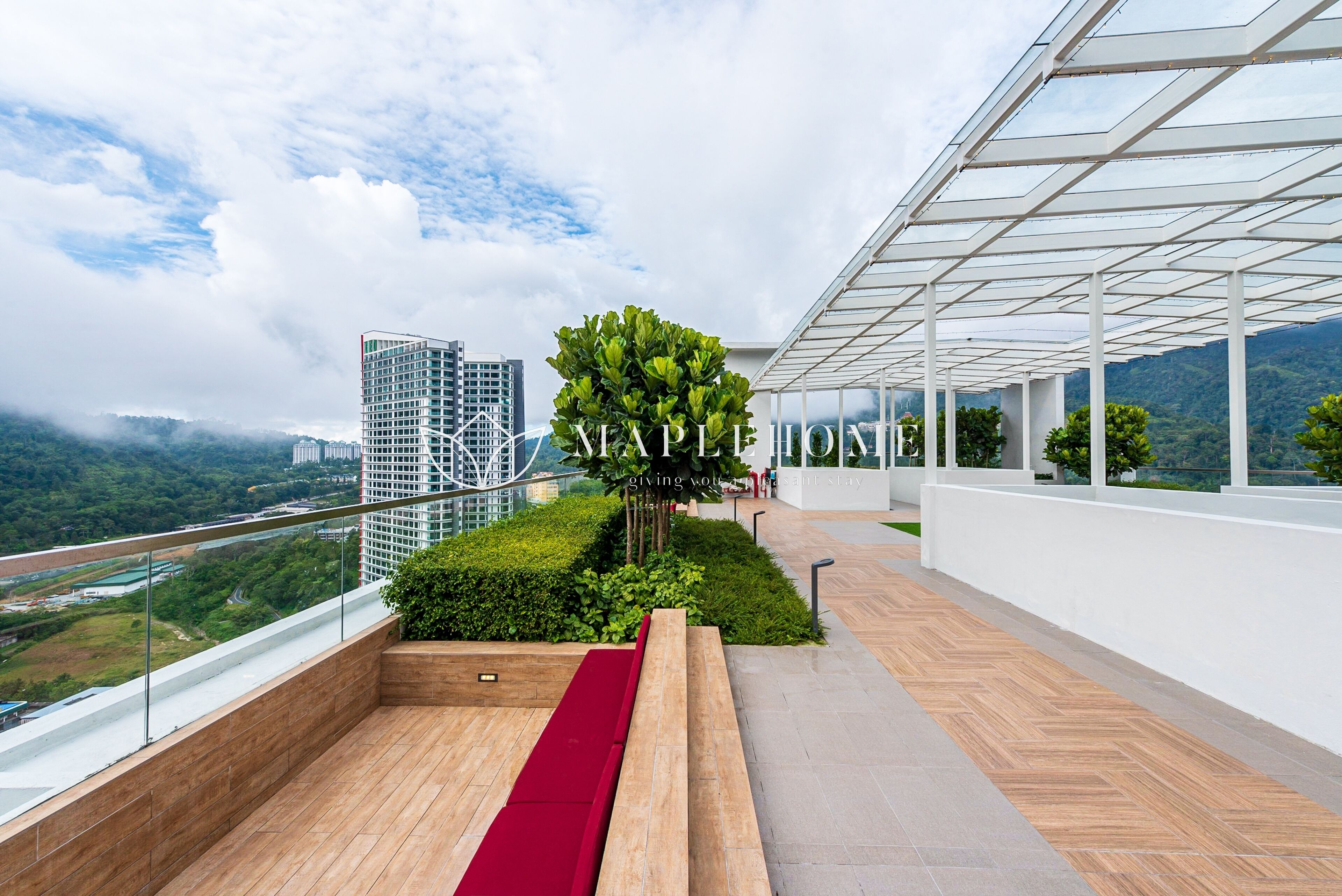 Una terraza en la azotea con barandilla de vidrio, un banco rojo y vistas a la ciudad y montañas.