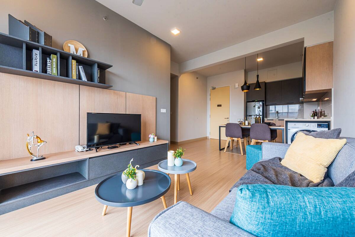 Un salon moderne avec un téléviseur, un canapé, une table basse et un coin repas comprenant des chaises, avec une cuisine en arrière-plan.