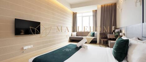 A modern hotel room with a bed, a desk, and a television mounted on the wall.