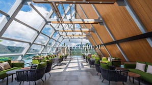 Un moderno salón en la azotea con mobiliario verde y negro, ventanas amplias y vista al agua.
