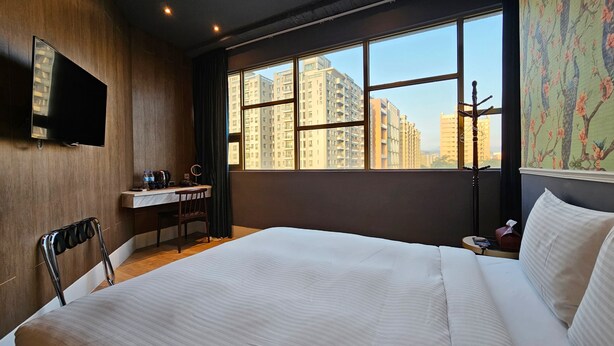 A hotel room with a bed, a desk, a chair, a TV, and a window with a city view. - Modern Inn (Taichung)