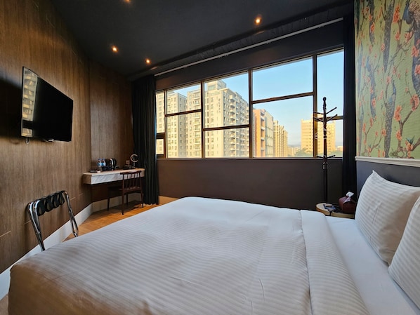 Habitación de hotel con cama, escritorio, silla, televisor y ventana con vista a la ciudad.