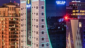 A modern hotel with a distinctive curved glass facade and illuminated signage. - Jouri A Murwab Hotel (Doha)