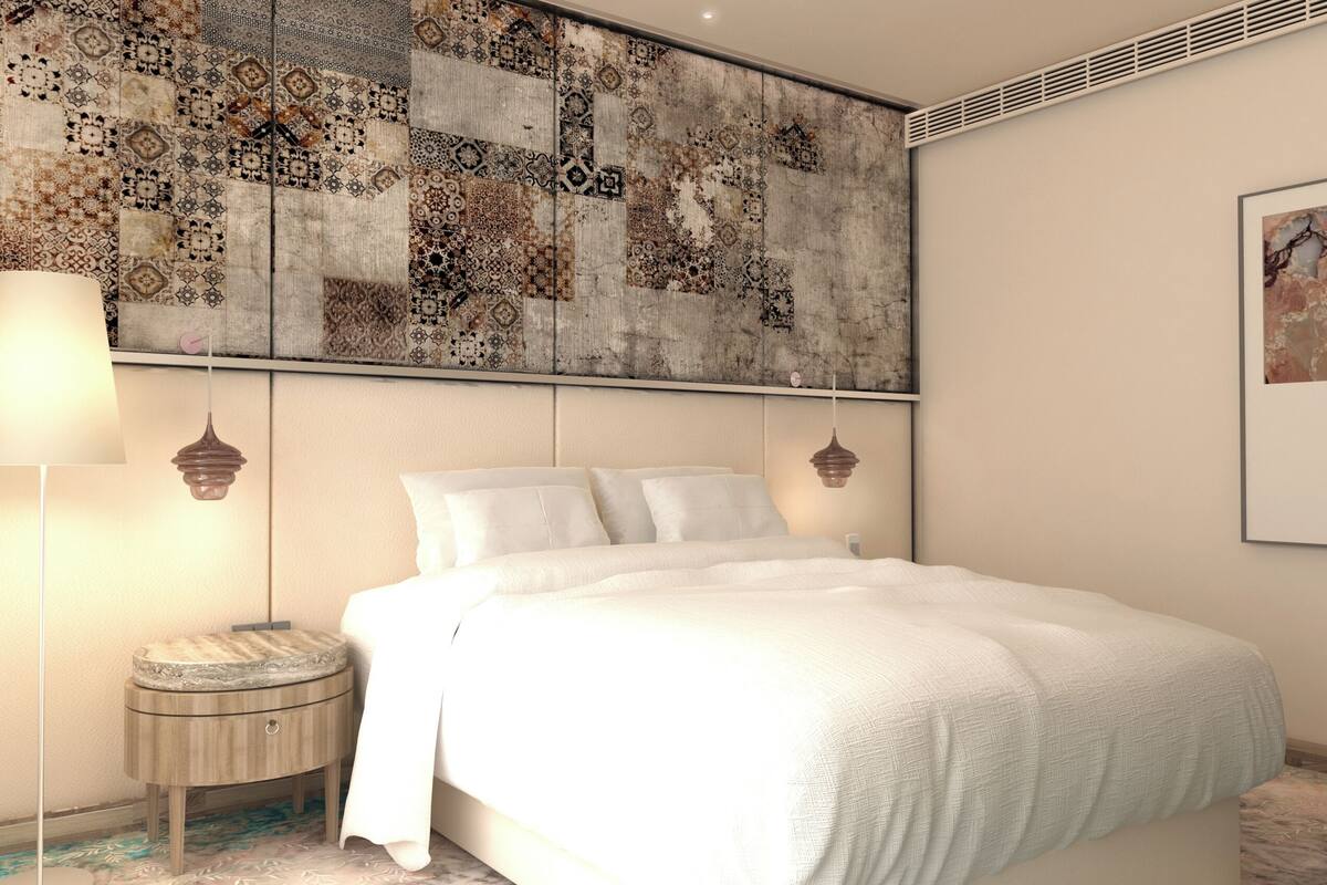 A bedroom with a large bed, a bedside table, a lamp, and a decorative wall hanging.