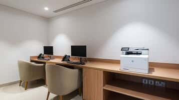 A modern office desk with two chairs, a computer, a phone, and a printer.
