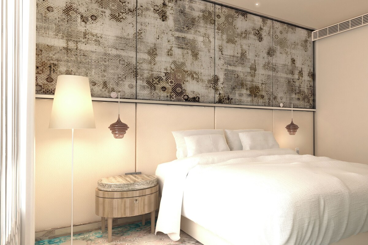 A bedroom with a bed, bedside lamps, a round nightstand, and a patterned headboard.