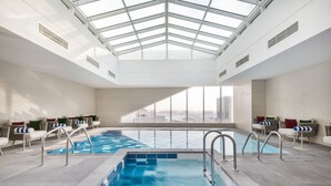 An indoor swimming pool with a glass ceiling, seating areas, and a view of the city. - Jouri A Murwab Hotel (Doha)