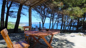 A wooden table and chairs set outdoors with a view of the sea and trees. - Romantic trullo with sea access and stunning views (house G) (Castro)