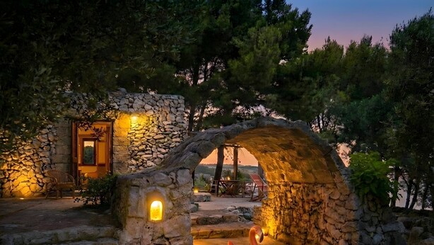 A stone archway leading to a cozy outdoor seating area with a swan-shaped inflatable decoration. - Romantic trullo with sea access and stunning views (house G) (Castro)