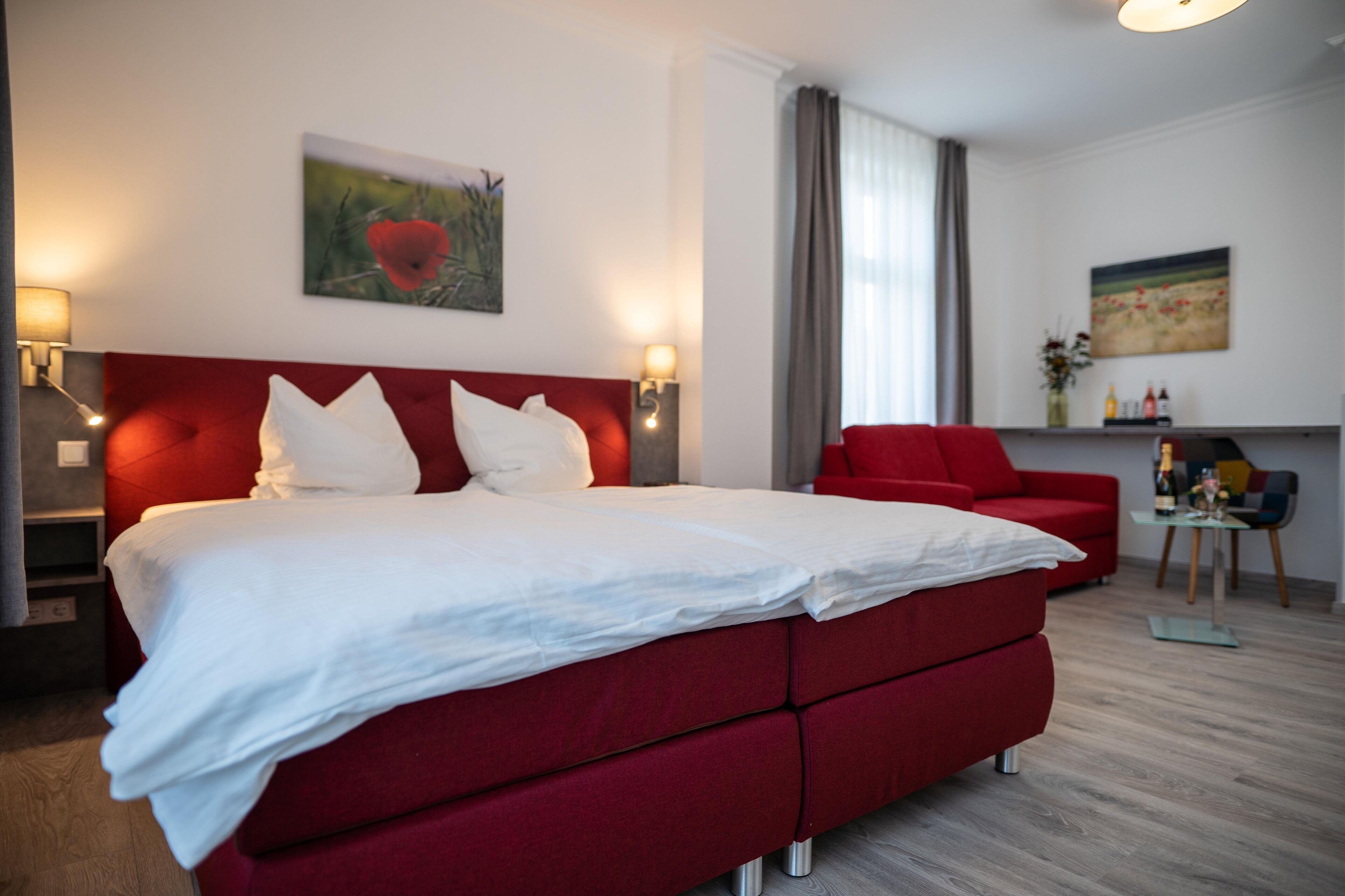 A hotel room with a large bed, a red sofa, a small table, and artwork on the walls.