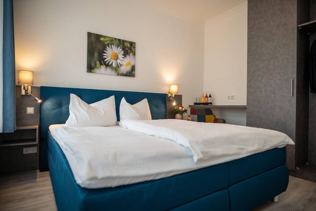 A neatly made bed with white linens, a blue headboard, and two bedside lamps.