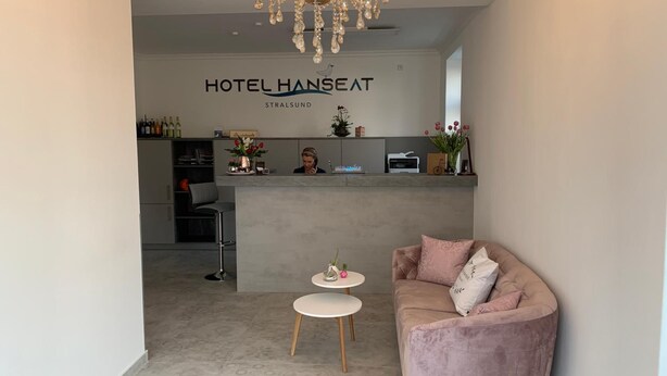 Un espace d’accueil d’hôtel au design moderne, comprenant un lustre, un comptoir d’accueil, un canapé et une petite table.