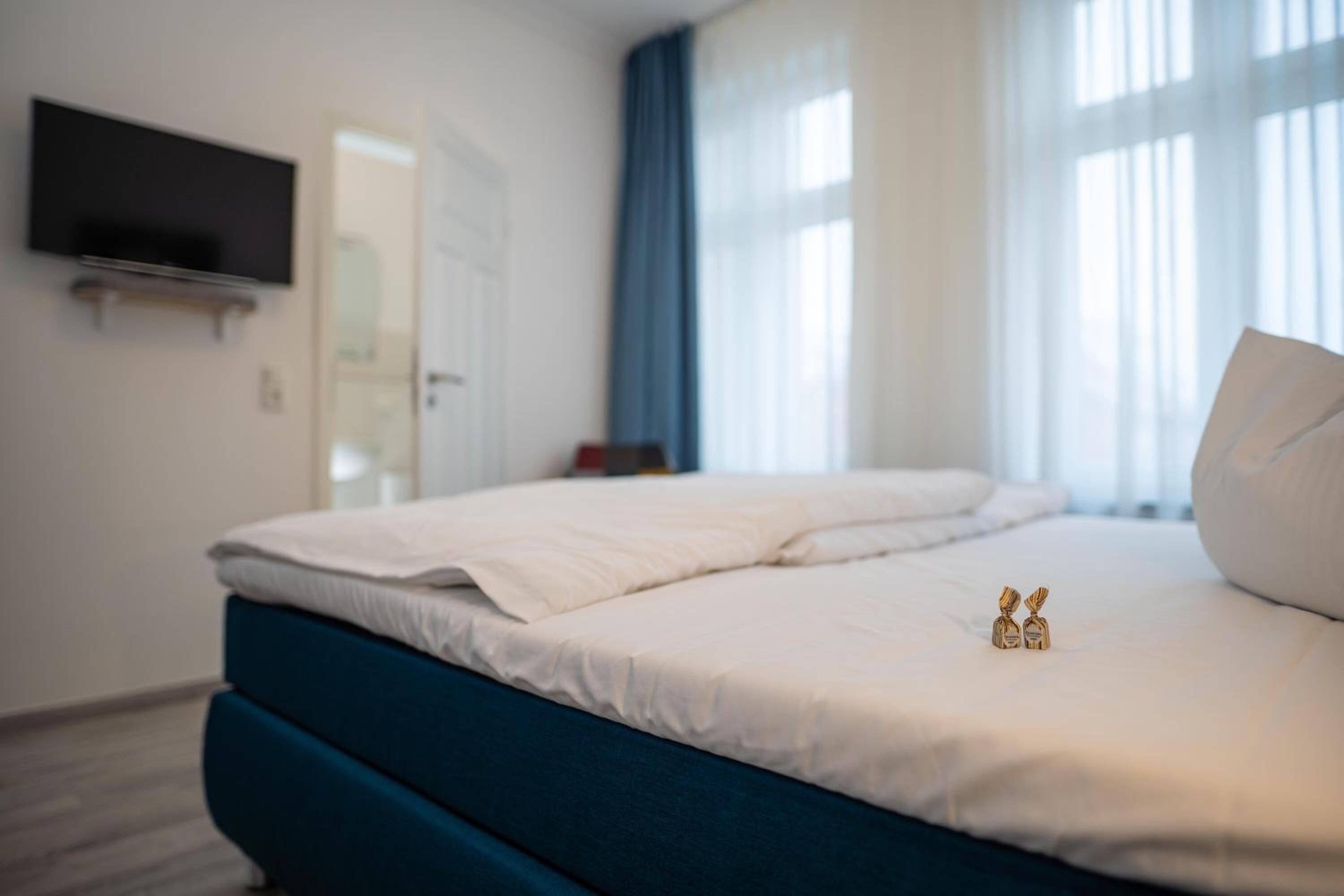 Una habitación de hotel con una cama, un televisor de pantalla plana montado en la pared y una ventana con cortinas.